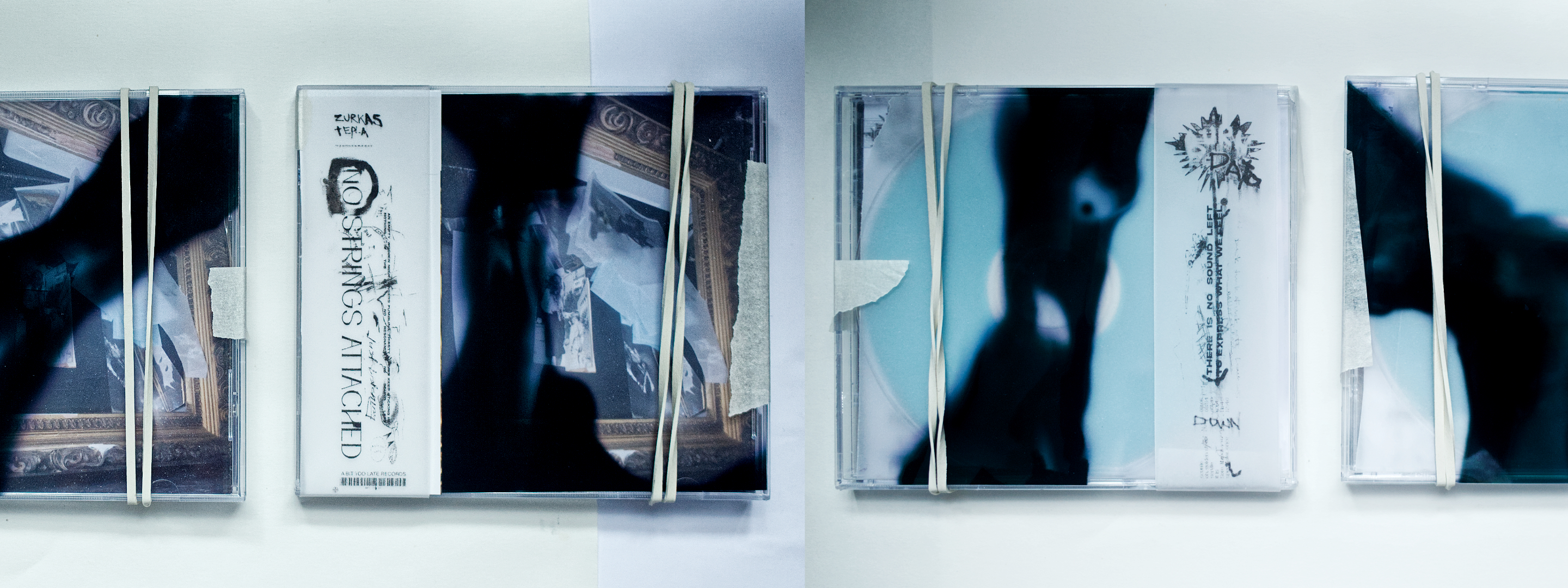 Four handmade CD copies laid on a wall, jewel cases wrapped with rubber bands and masking tape over printed vellum inserts